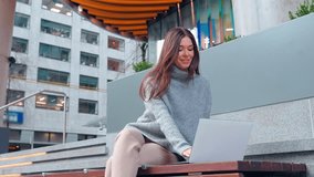 Young smiling happy business woman professional or student sitting outdoors on city street holding smartphone using mobile cell phone and laptop hybrid working or studying online outside office. - Powered by Shutterstock - Get 15% off with code: PIKWIZARD15