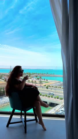 A girl sits on a chair on the balcony and looks at the sea, a girl relaxes on a chair looking at the sea from the balcony