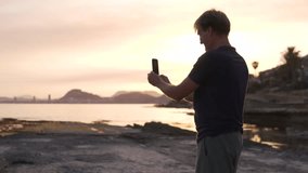 A man takes a panoramic photo of the sea at sunset on a mobile phone. Spain, Cabo de Huertas.
