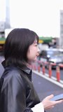 Vertical slow-motion video of a Japanese woman in her 20s walking around Gotanda Station, Shinagawa-ku, Tokyo in winter while operating her smartphone