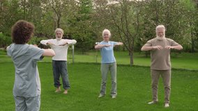 Full footage of young female nurse in uniform standing in garden of retirement home in front of group of elderly pensioners, demonstrating physical exercise, and senior people repeating - Powered by Shutterstock - Get 15% off with code: PIKWIZARD15