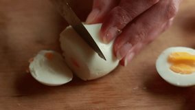 A close-up stock video capturing the hands of a woman delicately slicing a boiled egg on a wooden cutting board, showcasing the simplicity and precision of meal preparation.
