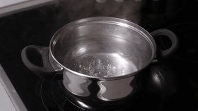  A close-up stock video capturing the process of water boiling in a pot on the stove, with emphasis on the bubbling and steam, set on a wooden board