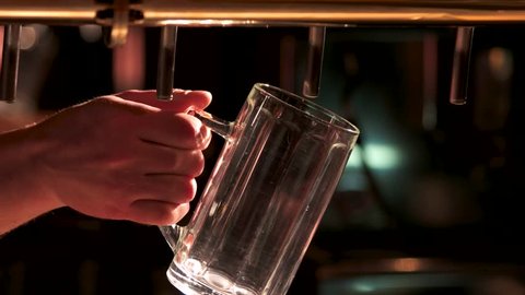 Man pours beer into a glass. Bartender's hand pouring pint of beer behind the bar. Drops of beer out of beer tap.: film stockowy