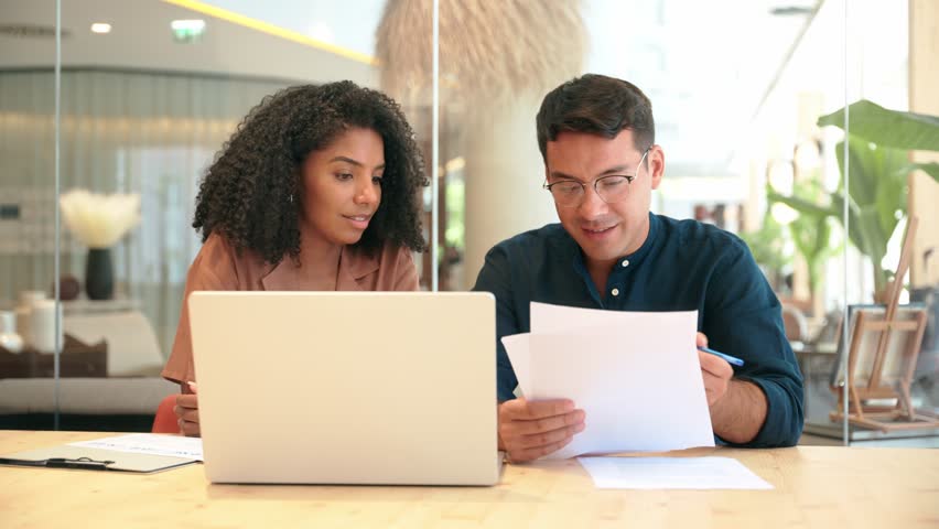 Diverse professional partners using laptop discussing document in office. Business team of two advisors, employees man and woman, manager and client talking on financial report working at work meeting