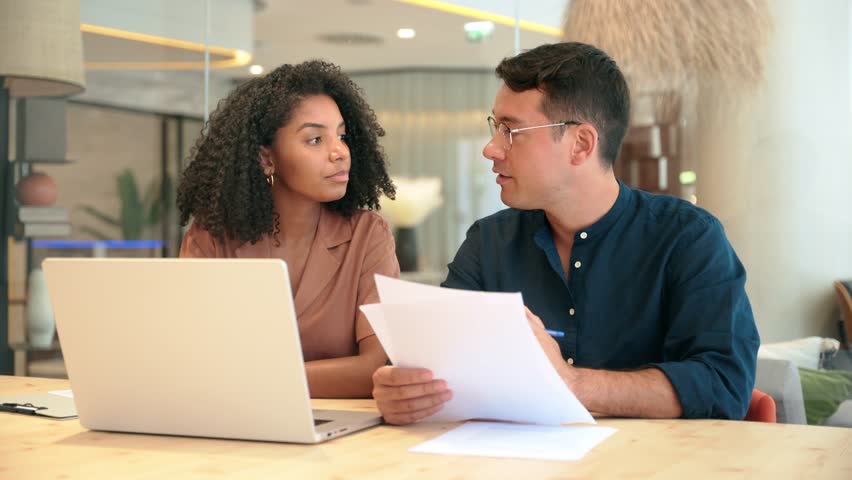 Diverse professional partners using laptop discussing document in office. Business team of two advisors, employees man and woman, manager and client talking on financial report working at work meeting
