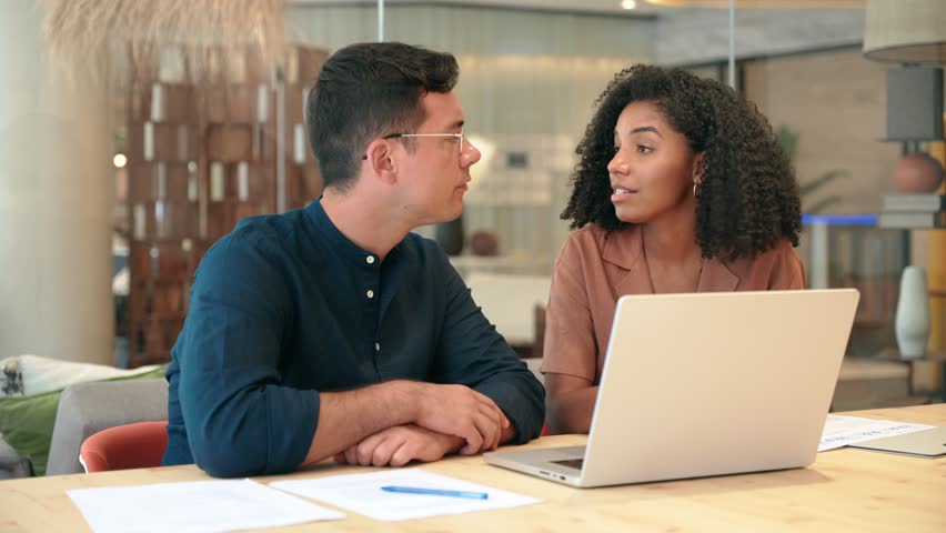 Two busy business people man and woman working on computer discussing online project at work. Diverse professional workers team talking on financial technology or marketing data using laptop in office