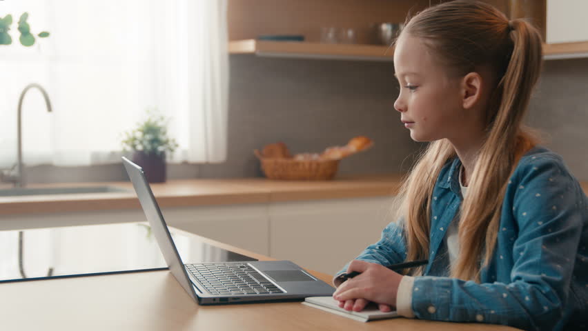 Moving camera Caucasian kid girl schoolgirl listen online lesson school class at home writing homework. Quarantine distant education. Child daughter studying remote with laptop e-learning at kitchen Royalty-Free Stock Footage #3484212709