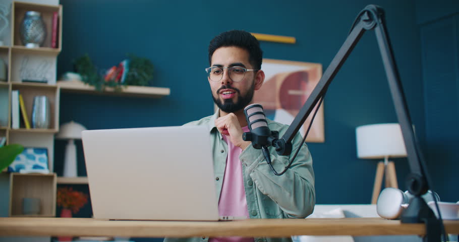 Confident man hosting podcast from home studio with modern microphone, laptop, on-air sign. Blogger recording voice for vlog, live streaming blog and sharing information with online audience. Royalty-Free Stock Footage #3484222021