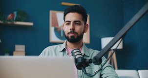 Young cheerful man recording podcast using laptop at home studio, broadcasting interview using microphone. Social media influencer interacting with audience. Content creator, marketing concept.