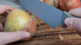 The fingers of a person peeling and cutting an onion over a wooden board with shallow focus.