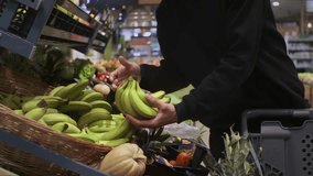 The hand or palm of a man or woman takes a bunch of bananas from a shelf in a store, puts them in a shopping cart. Vegetables or fruits are products in the store or supermarket - Powered by Shutterstock - Get 15% off with code: PIKWIZARD15