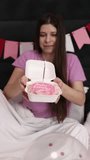 Millennial woman blows out candle  pink cake on her birthday decorated bedroom pink flags. Pink lilac T-shirt. Celebrating your birthday. Morning surprise. Vertical slow motion video