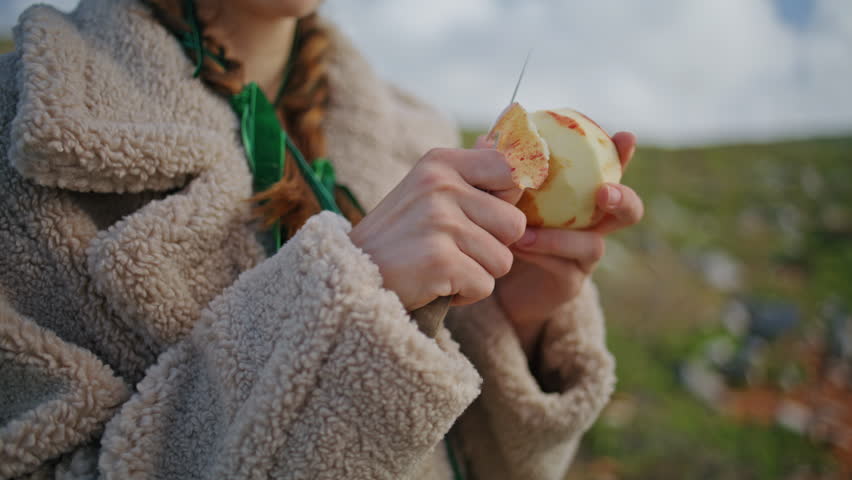Hands peeling apple skin on journey closeup. Woman preparing fresh healthy snack resting on mountain trip. Unknown gardener tasting checking seasonal harvest on green hill. Health balance dieting.