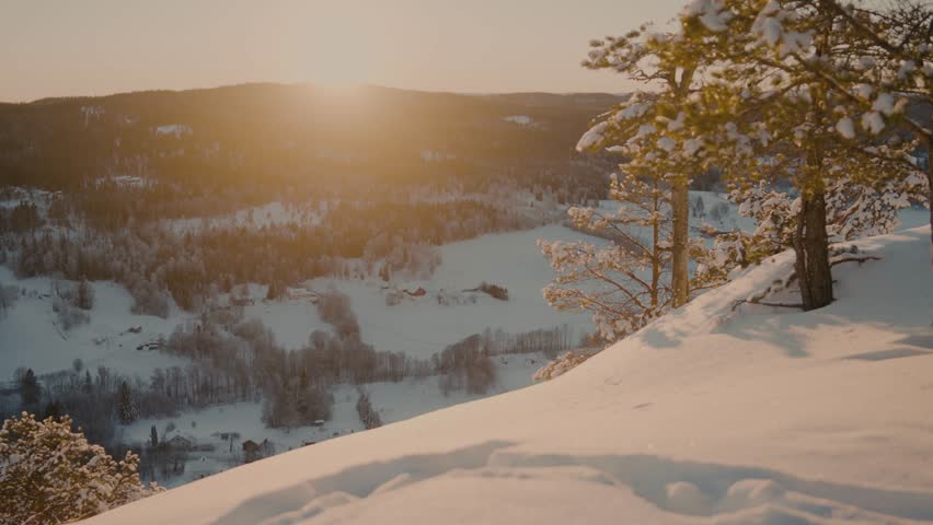 Sunset at the peak of a snowcovered mountain in Norway with a beautiful view of another mountain filled with trees and snow and a lot of colors