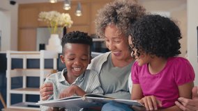 Grandfather joins grandmother sitting with grandchildren on sofa at home and they all read book together - shot in slow motion - Powered by Shutterstock - Get 15% off with code: PIKWIZARD15