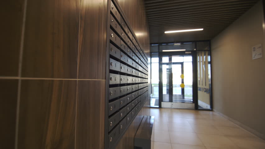 Numbered lockable metal mailboxes located in corridor of building. Rows of secure letterboxes match interior of building corridor