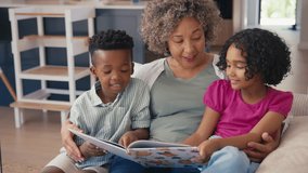 Grandmother sitting with grandchildren on sofa at home reading book together - shot in slow motion - Powered by Shutterstock - Get 15% off with code: PIKWIZARD15