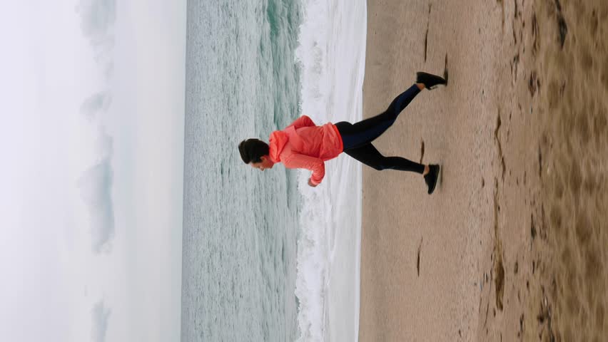 Woman running along coastline at stormy weather. Chubby female in sportswear jogging near seashore. Sport concept. Vertical video