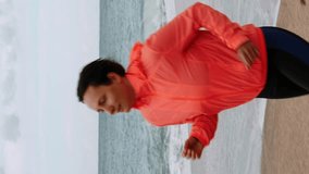 Portrait of woman in sportswear running on sand near sea. Chubby female jogging at seashore. Active lifestyle. Vertical video