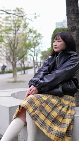 Vertical slow-motion video of a Japanese woman in her 20s sitting in a park around Gotanda Station, Shinagawa-ku, Tokyo in winter