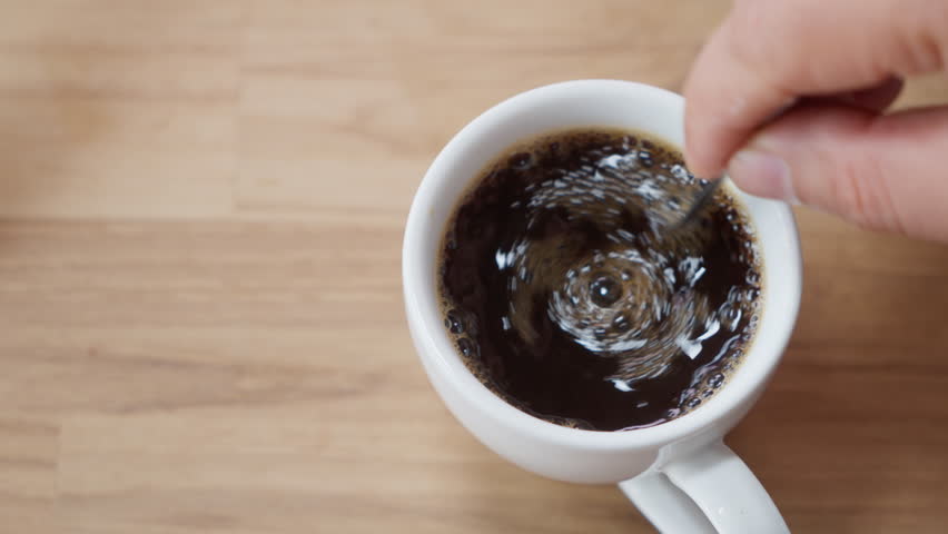 Top view of Person hand steering coffee in a cup with spoon. Breakfast morning of a cup hot black coffee on wooden background. footage b-roll Slow motion scene 4k. home making coffee. 