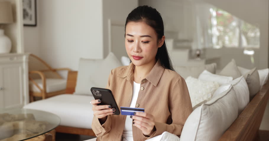 Asian woman using smartphone holds debit card do e-shopping at home, enjoy convenient and secure shopping experience, make easy mobile payment and transaction, feel satisfied with successful purchase Royalty-Free Stock Footage #3484619235