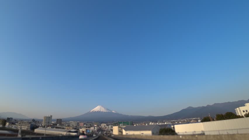 SHIZUOKA, JAPAN - MARCH 2024 : View of MOUNT FUJI (FUJISAN) and cityscape of Fuji city in sunset. Tallest mountain in Japan. 4K time lapse shot, dusk to night.
