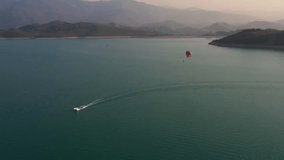 Man flying on parachute wide shot top view. Parachute flying over water with mountains on background. Parasailing in sea across seaside. 