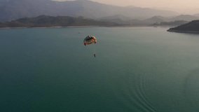 Man flying on parachute wide shot top view. Parachute flying over water with mountains on background. Parasailing in sea across seaside. 