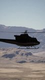 An old American military retro helicopter flying in the sky over a rugged mountain range.