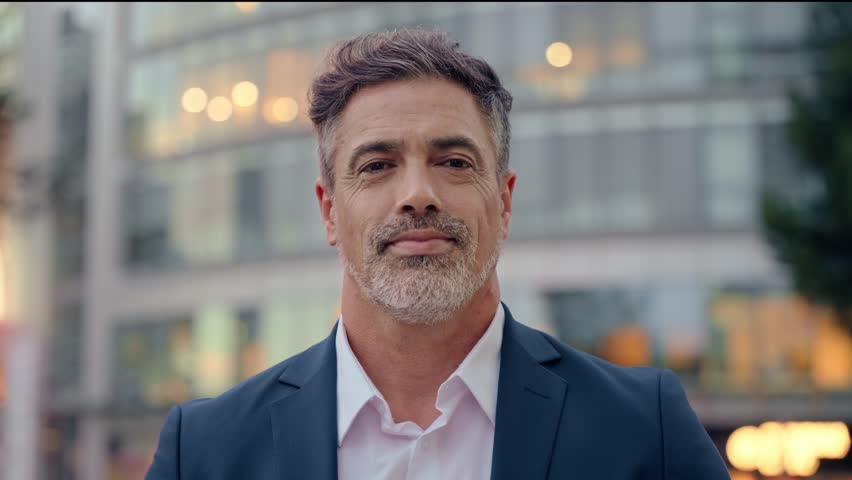 Mature hispanic senior business man standing on busy city street. Headshot close up portrait of Indian or latin confident good looking middle age male entrepreneur businessman happy smiling at camera.