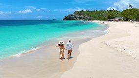 Elevated view of a couple with sunhats walks down a tropical beach with turquoise sea in the Caribbean, Antigua island - Powered by Shutterstock - Get 15% off with code: PIKWIZARD15