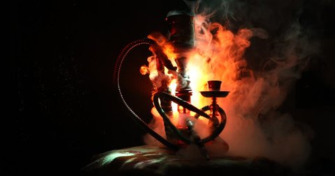 Hookah hot coals on shisha bowl on orange (like fire) clouds of steam on dark background. Stylish oriental shisha. Shisha Concept. On rotating display. 