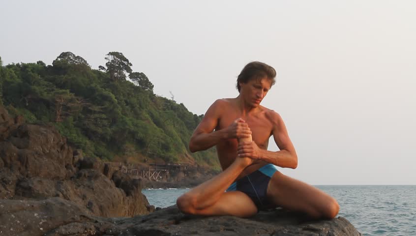 Young man doing yoga exercise on the deserted wild stone sea beach (HD)