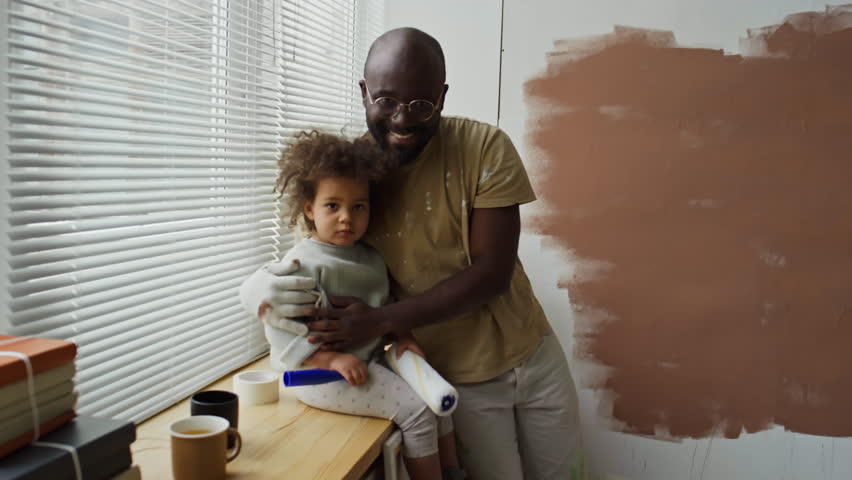 Portrait of caring African American father hugging his little Biracial daughter who sitting on windowsill and smiling while looking at camera during home renovation Royalty-Free Stock Footage #3484877173