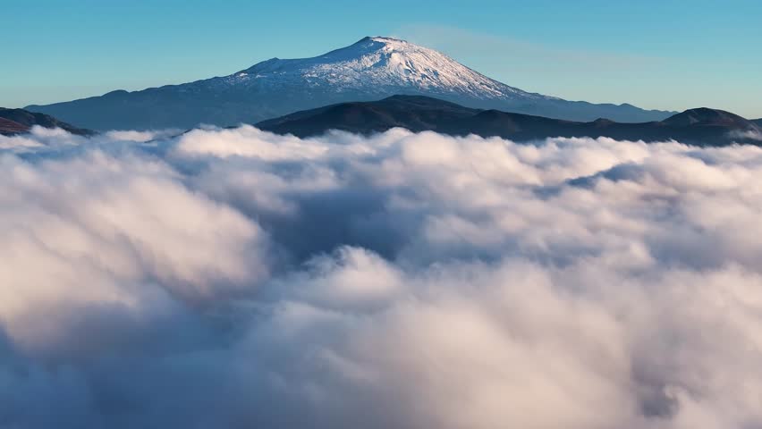 Aerial shot with drone of Etna above the clouds at dawn. Low clouds with a view of the Etna volcano in Sicily above the clouds. Etna in winter. Sicily in winter. Etna seen from the Nebrodi above Lake 