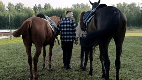 A young family is preparing to ride horses. Young pastime on a farm with horses. Family couple on the farm. Next to the horses are a man and a woman. view from the back - Powered by Shutterstock - Get 15% off with code: PIKWIZARD15