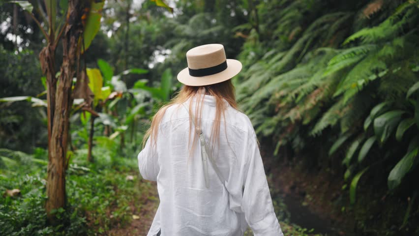 Carefree blonde woman in straw hat admire view mountain waterfall in wild nature. Girl tourist in hike, back view. Hiking, female carefree, tourism, summer vacation, national park journey concept.