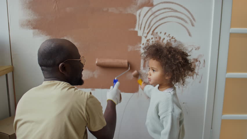 Rear footage of African American father and little cute Biracial daughter painting walls brown with paint roller, girl using mini roller Royalty-Free Stock Footage #3484943947