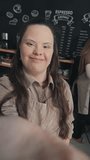 Vertical portrait of modern young female barista with Down syndrome recording video for blog inviting customers to coffeehouse