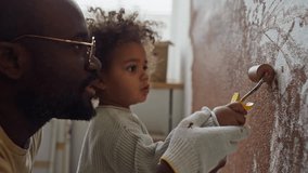 Side close-up of curious little Biracial girl helping her African-American father painting walls with mini paint roller while renovating flat - Powered by Shutterstock - Get 15% off with code: PIKWIZARD15
