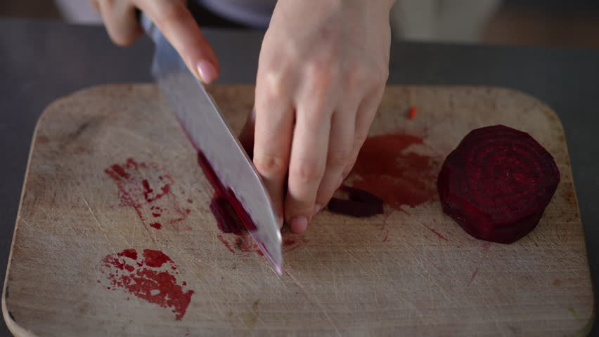 Close-up. Women's hands cut red peeled beet on a wooden cutting board with a kitchen knife into thin, long slices