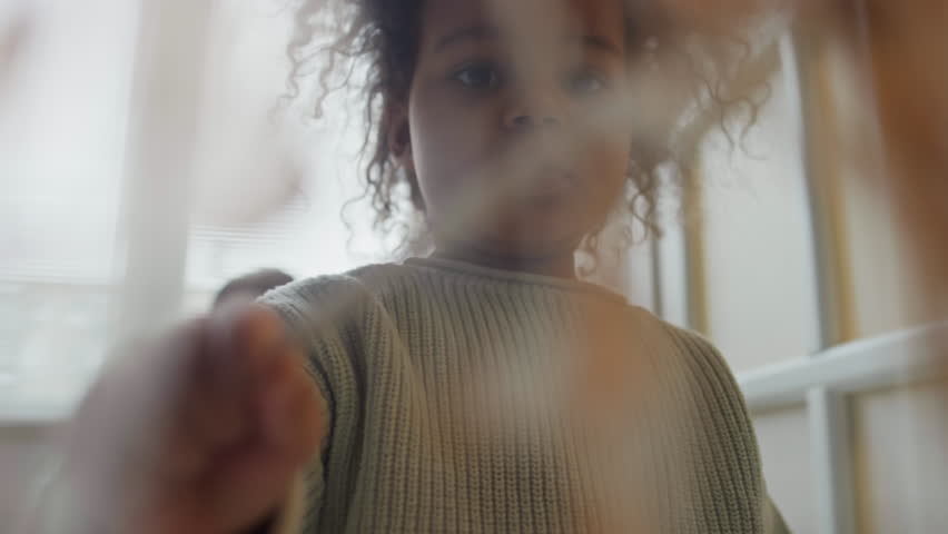 Through-glass footage of cute little Biracial girl with puffy hair painting transparent surface during room renovation Royalty-Free Stock Footage #3485103055