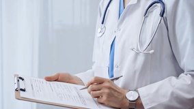 Female doctor taking notes on clipboard. Close-up of a unrecognizable female healthcare professional writing and filling um medication history records form while standing straight in clinic