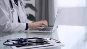 Stethoscope and medical clipboard are lying on the glass table while doctor woman is working with laptop computer on the background. Medicine and pharmacy concept