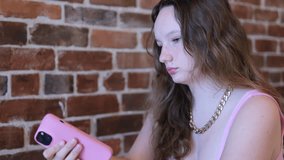 A young attractive woman uses a smartphone and frowns and looks at it with displeasure in the apartment. Gadget addiction
