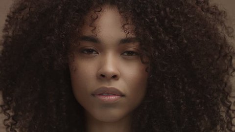 front portrait of black woman with huge curly hair looking at camera. ideal skin concept. Beige tones natural makeup