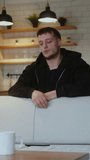 Vertical video. Young man leaning over the back of the sofa feeling bored, suffering from depression.