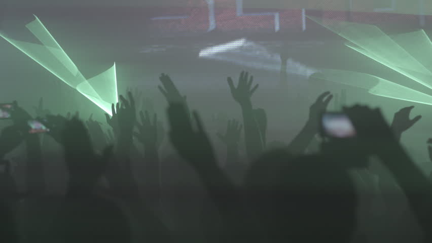 An atmospheric shot capturing a cheering crowd with hands raised against a dynamic backdrop of geometric laser lights at an evening entertainment event